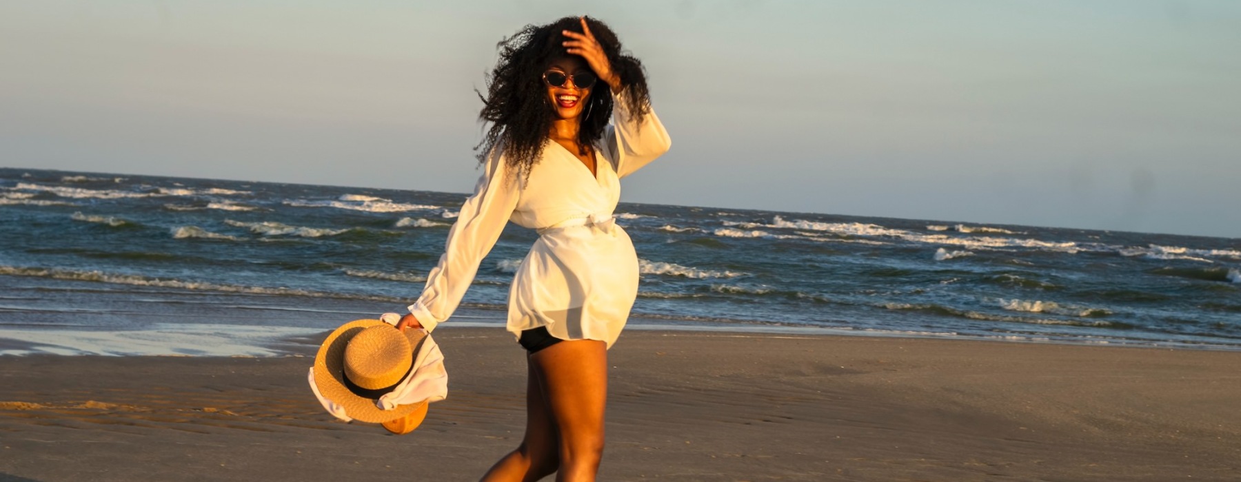 a woman walking on the beach with a hat in her hand