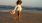 a woman walking on the beach holding a hat